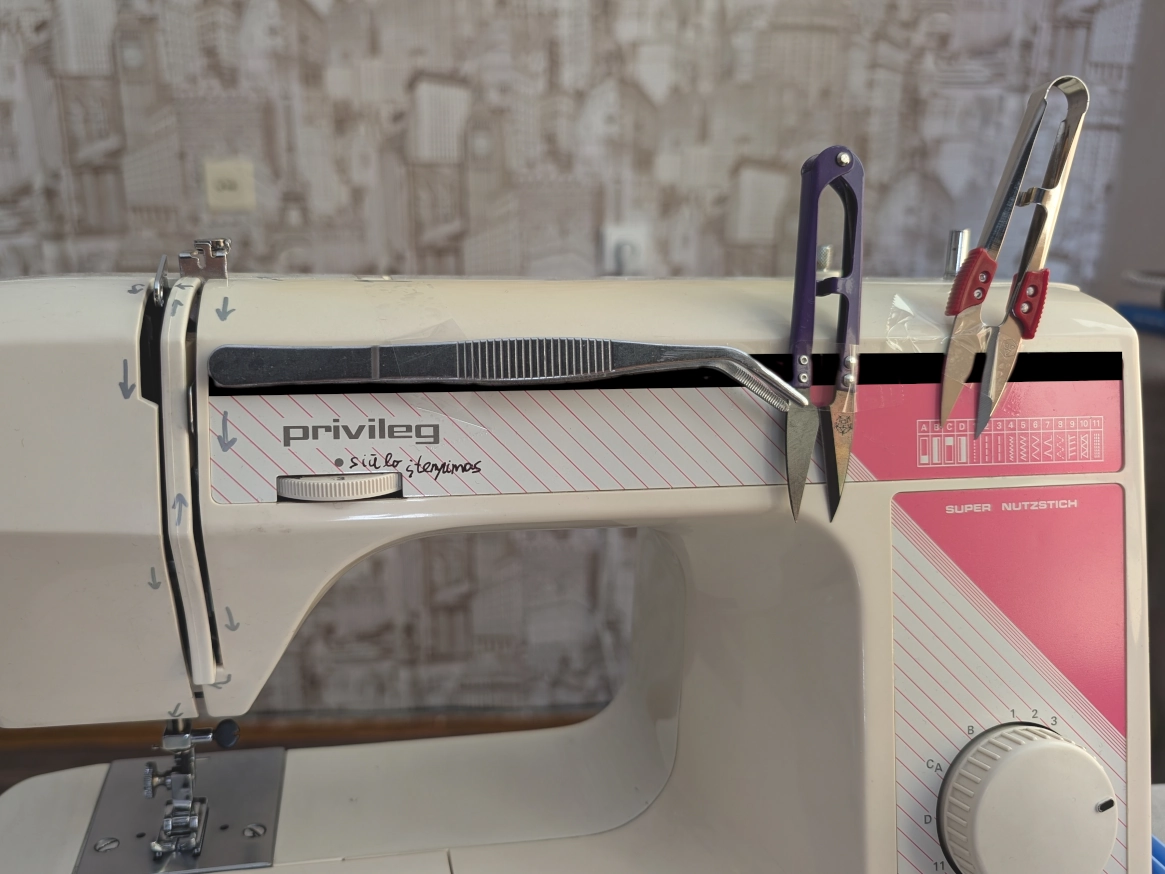 Siuvimo mašinos priekis su priklijuotais įrankiais ir nupiešta magnetine juosta.