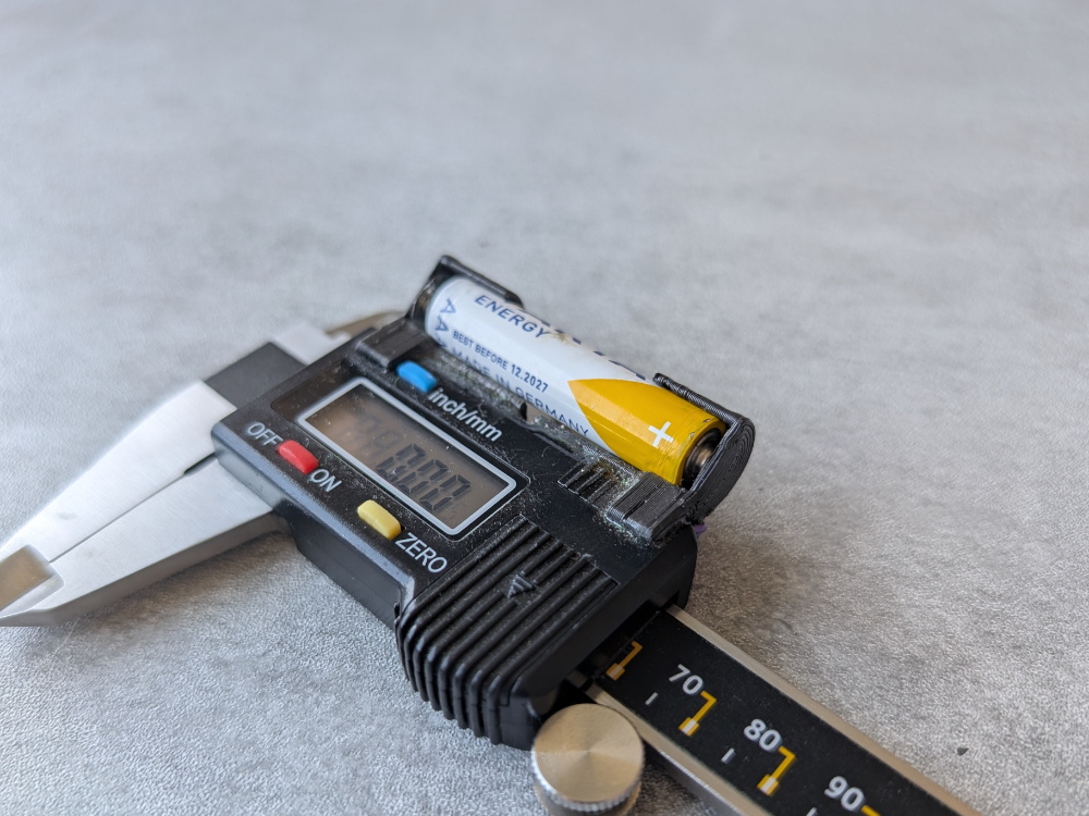 Prie slankmačio priklijuotas trijų A baterijos laikiklis.